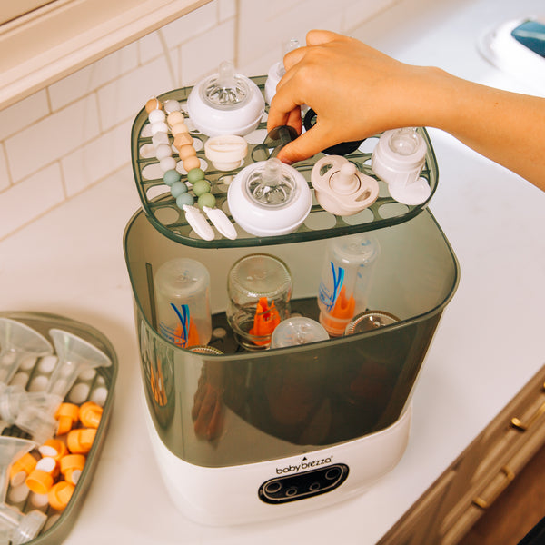 a hand lifting the top rack of the Baby Brezza SDA filled with parts and bottles - product thumbnail