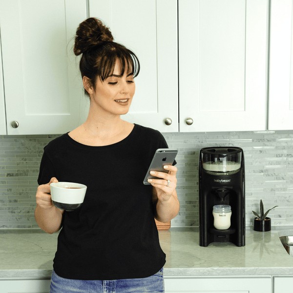 Baby Brezza FPA Wifi dispensing a bottle while a mother enjoys a coffee - product thumbnail